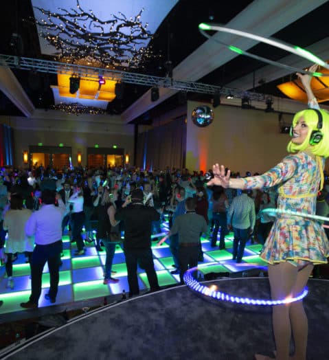A performer spins lighted hula hoops onstage at one of our corporate events, booked by our talent booking services.