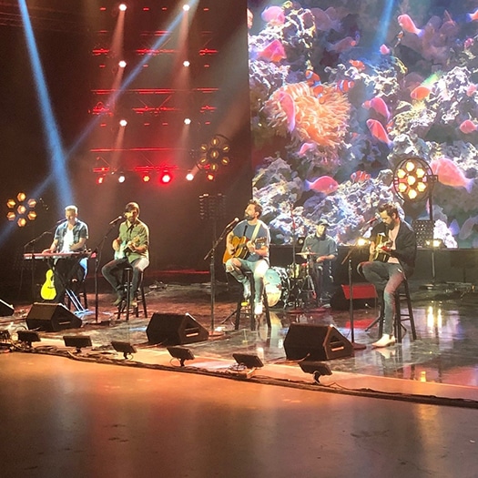 A band performing on stage with lighting overhead for virtual event production